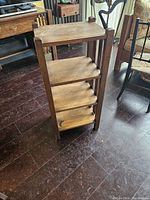 Side angle of solid wood bookshelf/plant stand showing four shelves and vertical slat sides.