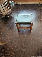 Front view of the antique Empire style black leather ottoman showing wood frame and leather top with nailhead trim.