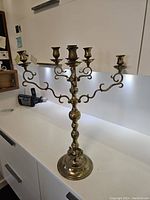 Front view of the vintage solid brass candelabra showing six candle holders on ornate curved arms and sturdy round base on white countertop.