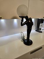 Full view of the black figurative lamp standing on a kitchen counter, showing the entire lamp and the globe light.