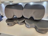Four gray contoured ergonomic seat cushions arranged on a white surface showing front and side views