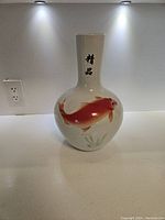 Front view of the porcelain vase showing a large red-orange goldfish and Chinese characters on the neck.
