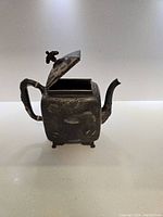 Front and side view of square silver plated teapot with bamboo style handle, spout, and floral embossing. Hinged lid is closed.
