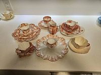 Overview of 18 piece assortment including cups, saucers, plates, and creamer arranged on countertop