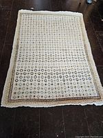 Full view of the rectangular handcrafted area rug laid flat on dark wood floor showing pattern and condition.