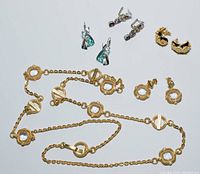 Photo showing all jewelry pieces together: multiple pairs of earrings and a long gold-toned chain necklace with square faceted stones and a Rebecca logo clasp.