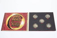 Red booklet packaging opened displaying five silver-tone coins in a black foam insert, showing front side with character engravings.