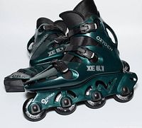Side angled view of the paired inline roller blades showing the Oxygen XE 5.1 branding, metallic green shell, black mesh inner, white wheels, and power braking system on heel.