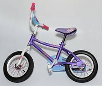 Full side profile of the toddler girls purple bicycle showing frame, wheels, seat, pedals, and grips.