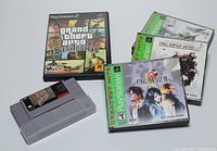 Photo of PlayStation 2 game discs and two Super Nintendo cartridges including Grand Theft Auto: San Andreas, Final Fantasy Anthology, Final Fantasy VIII, Sim City, and Star Wars.