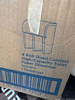 Photo of cardboard box with a blue line drawing and description of the 4 roll quad coreless high-capacity stainless steel toilet paper dispenser.