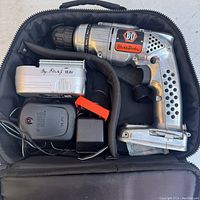 Top-down view of cordless drill, battery pack, battery charger, and carrying case interior showing layout and condition.