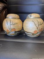 Front view of two brass enameled painted lidded ginger jars showing floral and branch designs.