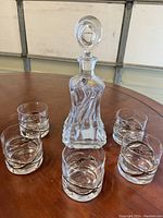 Full view of one crystal decanter with stopper surrounded by six matching tumblers on a table.