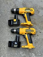 Photo of two Dewalt cordless drills with two batteries on concrete surface.