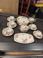 Top-down shot of set including cups, saucers, covered serving dish, sugar bowl, cream pitcher, and tray with floral and gold decoration