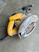 Photo of used DeWALT circular saw showing yellow handle and power cord on concrete floor.