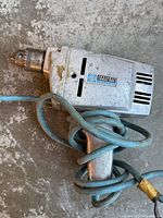 Photo showing the full drill in silver metal casing with blue power cord wrapped around the handle.