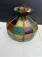 Side and angle view of stained glass ceiling light showing multicolored textured glass panels with brass frame and wiring attached.