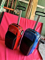 Side view showing the red and blue Range Rover suitcases with extended trolley handles and wheels, placed upright.