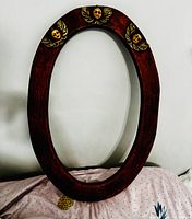 Front view of the wooden oval mirror frame showing reddish-brown textured finish and three gold-colored angel faces with wings.
