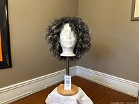 Front view of the grey tipped curly synthetic wig on a display stand showing full hair volume and curl pattern.