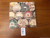 Photo of puzzle box cover showing various decorative teacups and saucers arranged in a collage style against a wooden surface with a MaxSold lot number.