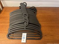 Stack of 31 black IKEA plastic wide hangers laid on a wooden surface.
