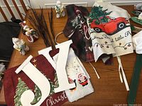 Photo showing all items: two wooden initials, two Christmas aprons, two hand towels with holiday embroidery, red Christmas placemats, and battery operated twigs