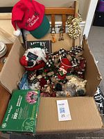Box containing mixed Christmas decorations including hat, figurines, ornaments and lights all visible