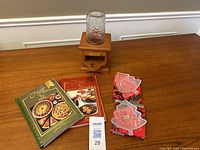 Wooden jelly bean dispenser with glass jar and four small candy dishes on wooden surface with two cookbooks in background.