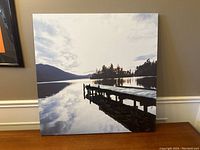 Full view of the 60cm x 60cm square stretched canvas showing a dock extending into a calm lake with distant trees and hills reflecting in the water.