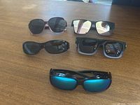 Five pairs of over prescription glasses sunglasses displayed on a wooden surface varying in frame shape and lens tint.