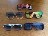 Five pairs of sunglasses laid on a wooden table showing varying lens colors and modern frames.