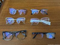 Top-down view of six optical frames arranged in two rows on a wooden surface, showing color and style variety.