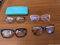 Five pairs of optical glasses and one blue hard case displayed on a wooden surface.