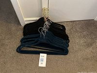 Set of velvet hangers laid on the carpet, showing stacked blue and black hangers with golden metal hooks.