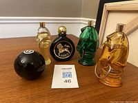 Full view of five vintage men’s cologne and aftershave bottles including horse head-shaped bottles, eight ball bottle, and Aries decanter.