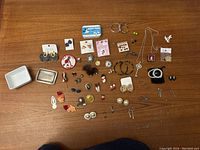 Wide shot of the assortment of jewellery items including earrings, brooches, pins, small jewellery tray and a small box.