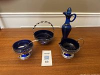 Top-down view of the vintage blue cobalt glass creamer, sugar bowl with spoon, and candy dish with silver-tone holders placed on a wooden table.