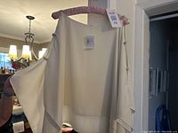 Front view of cream-colored elegant women's top on padded hanger showing flowy fabric and long sleeves.