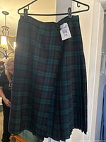Full view of the blue and green tartan skirt on a hanger showing pleats and waistband with size tag