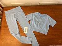 Photo showing the full yoga two-piece laid flat on wooden table: baby blue crop top and leggings.