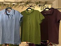 Three women's golf shirts - medium blue, grass green, purple - hanging side by side, showing front view and collars