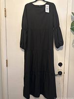 Front view of black long sleeve ruffled lightweight dress hung on a hanger showing overall design and length.