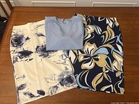 Photo of all three clothing items laid flat on table: white floral skirt, navy floral skirt, and light blue blouse folded and placed on top
