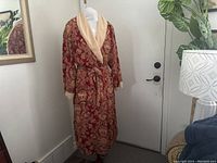 Full view of the vintage wrap house coat on a dress form, showing the red paisley and floral pattern and beige terry cloth collar lining.