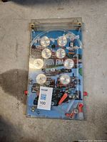 Full view of antique tabletop pinball game with clear plastic cover and colorful racing car theme background.