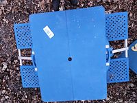 Top view image of blue folding picnic table with four attached lattice metal seats and carrying handles, placed outdoors on leaf-covered ground.