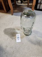 Clear glass hat holder shaped like a human head placed on concrete floor next to a lot number tag.